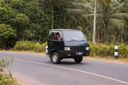 Mobil mini pickup hitam lucu melaju di jalan pedesaan dengan latar pohon kelapa