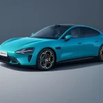 Tampak samping depan mobil listrik terbaru Xiaomi SU7 berwarna biru yang sedang melaju di jalan raya aerodinamis.